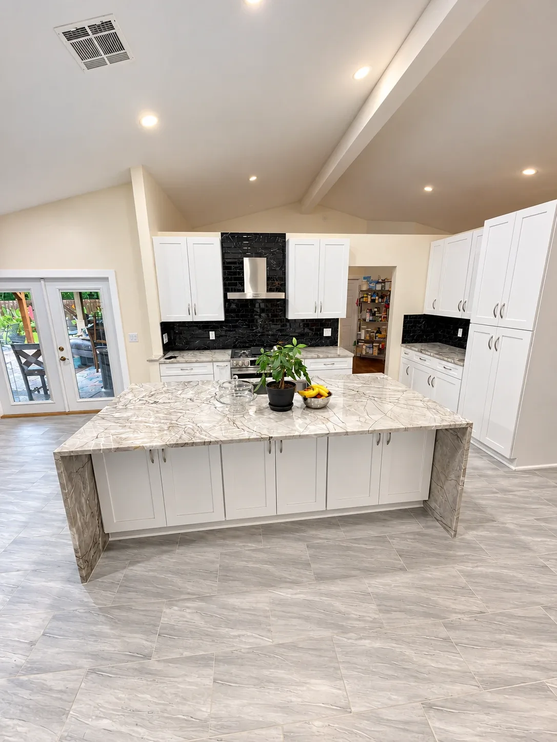White shaker kitchen with black backsplash, quartzite waterfall island and gray porcelain tile floor, Avondale Jacksonville