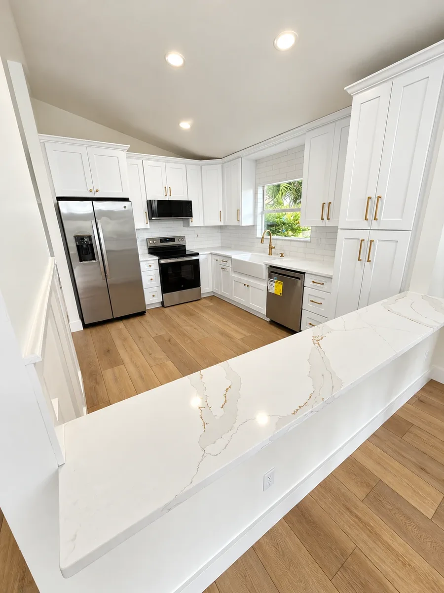 After: remodeled kitchen with white shaker cabinets, quartz peninsula and light oak luxury vinyl plank flooring in St. Augustine Beach, FL