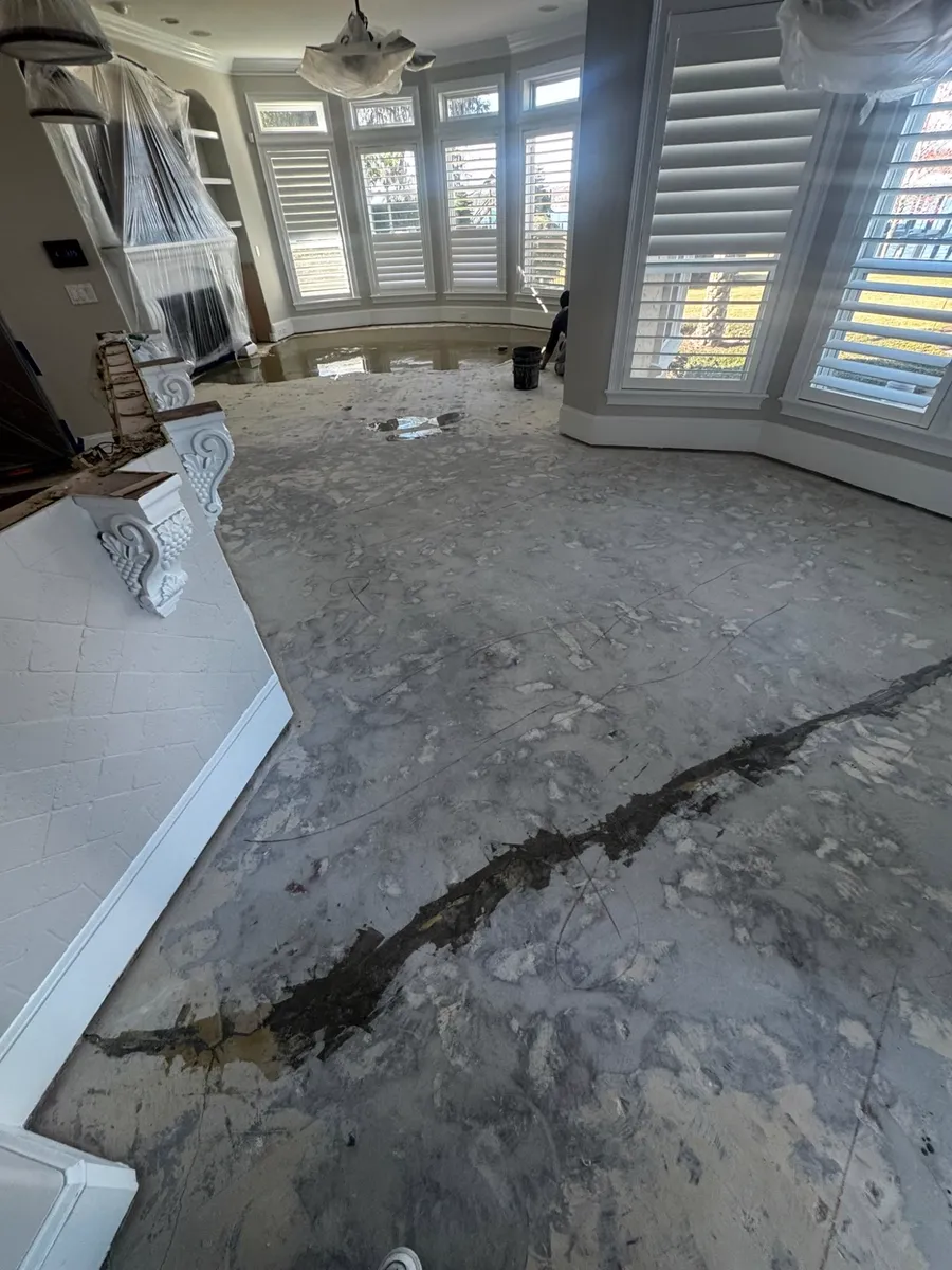 Before: cracked concrete subfloor with old flooring adhesive in a San Marco living room